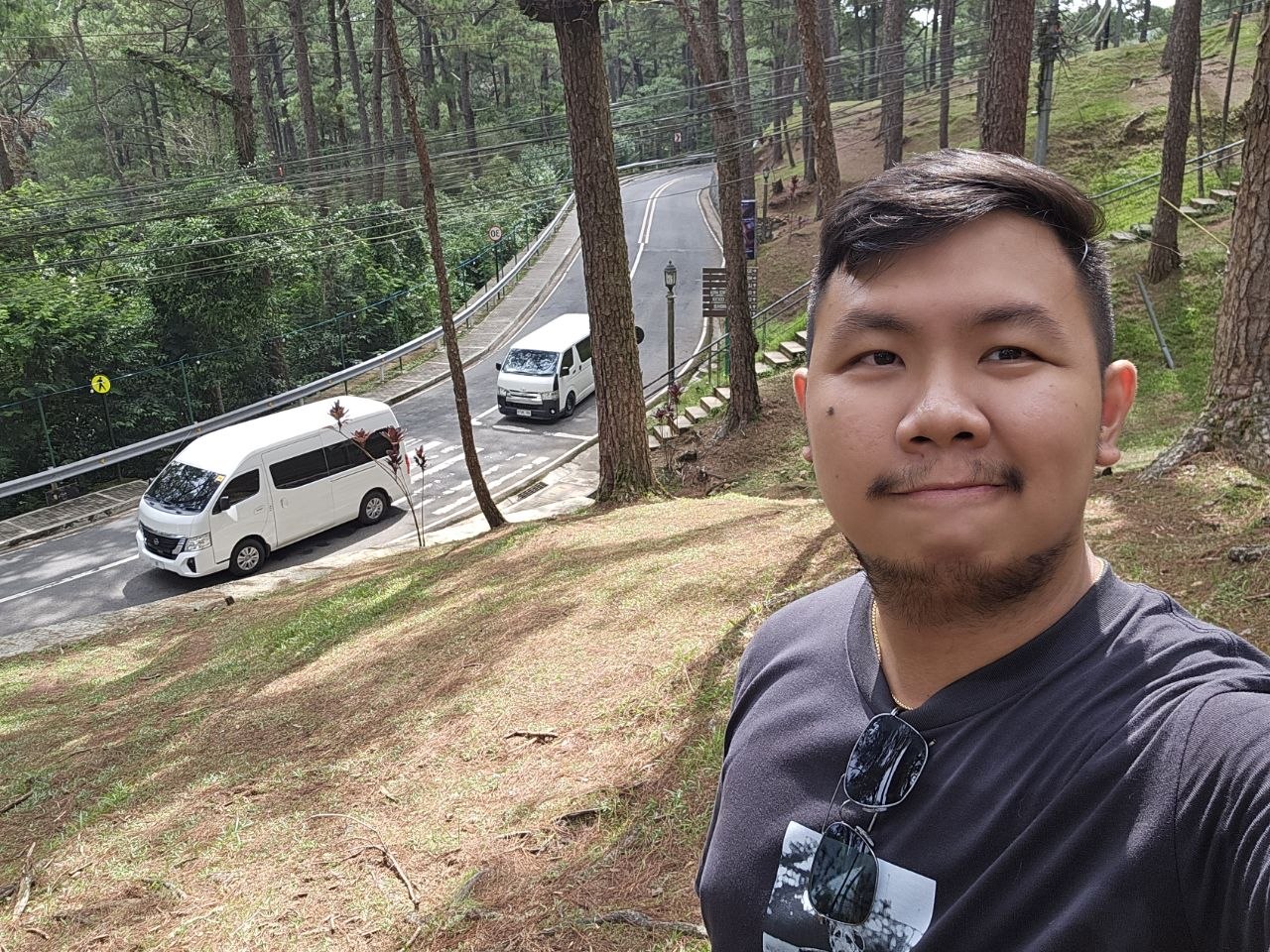 Norman standing among pine trees beside a winding road